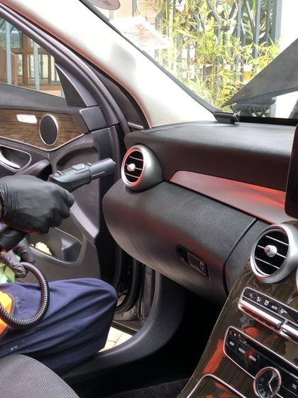 Gloved hand steam-cleaning the air vents of a Mercedes C-Class dashboard