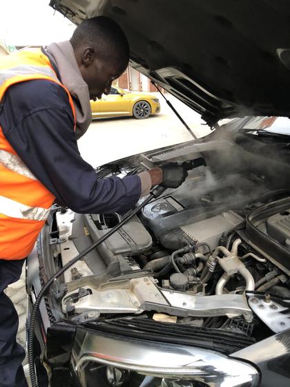 Detailer steam-cleaning an engine bay, steam rising