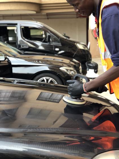 Detailer machine-polishing the bonnet of a black Mercedes, the building reflected in the paint